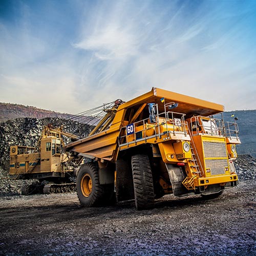 A large yellow dump truck parked on top of a gravel road.
