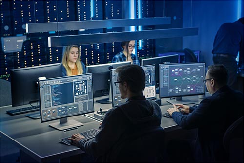 A group of people sitting at computers in front of screens.