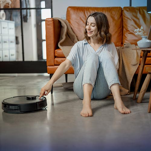 A woman sitting on the floor with a robot vacuum.