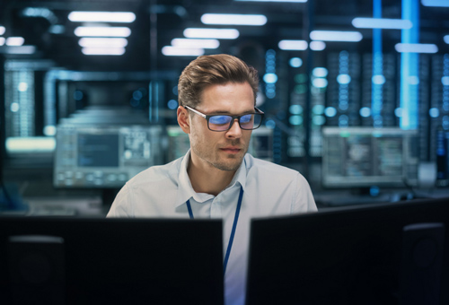 A man sitting at his desk looking at two computers.
