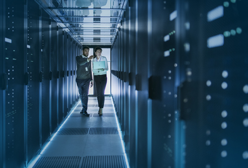 Two men walking in a hallway of server racks.