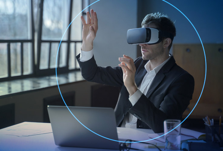 A man wearing virtual reality glasses in front of a laptop.