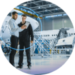 Two men standing in a hangar looking at something on their phone.