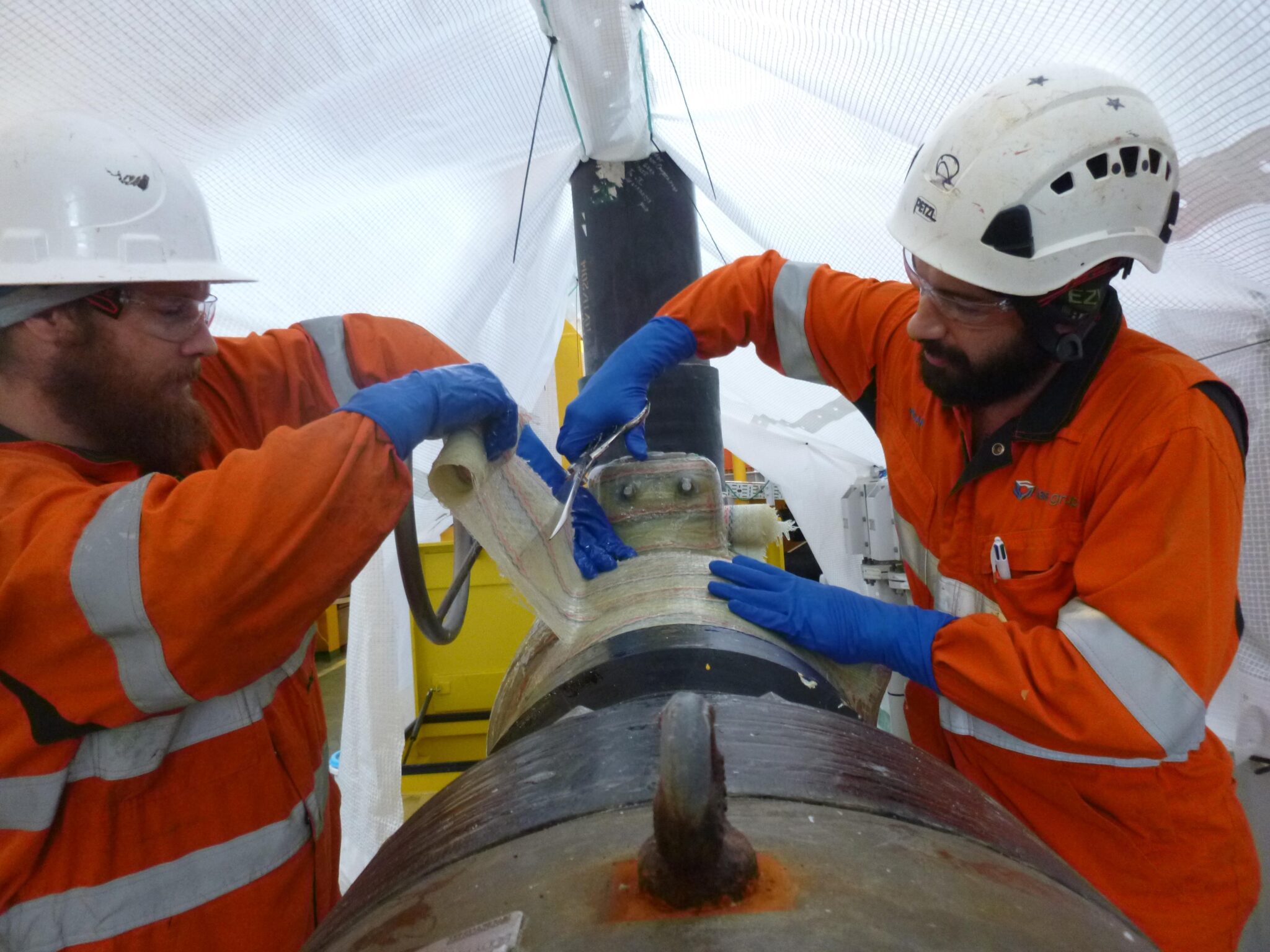 Two men in orange jackets working on a pipe.