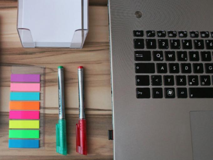 A laptop with sticky notes and pens on the desk.