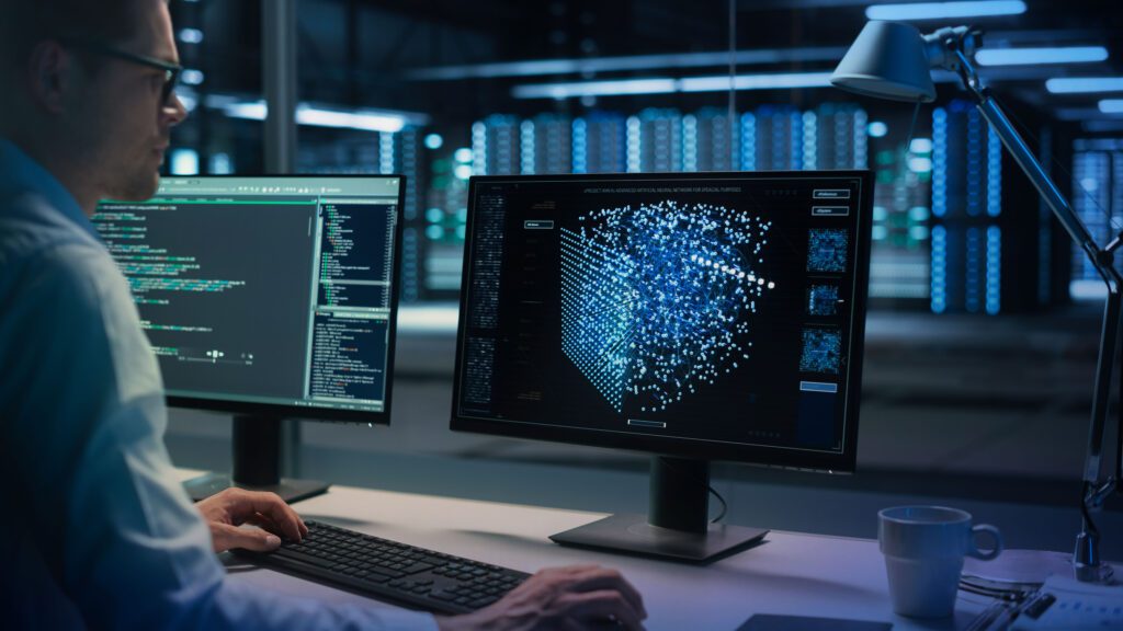A person sitting at a desk with two computers.